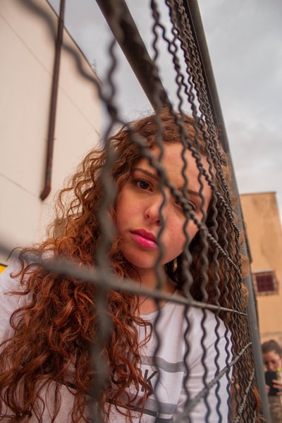 During the day, a woman wearing a white shirt on brown metal fence
